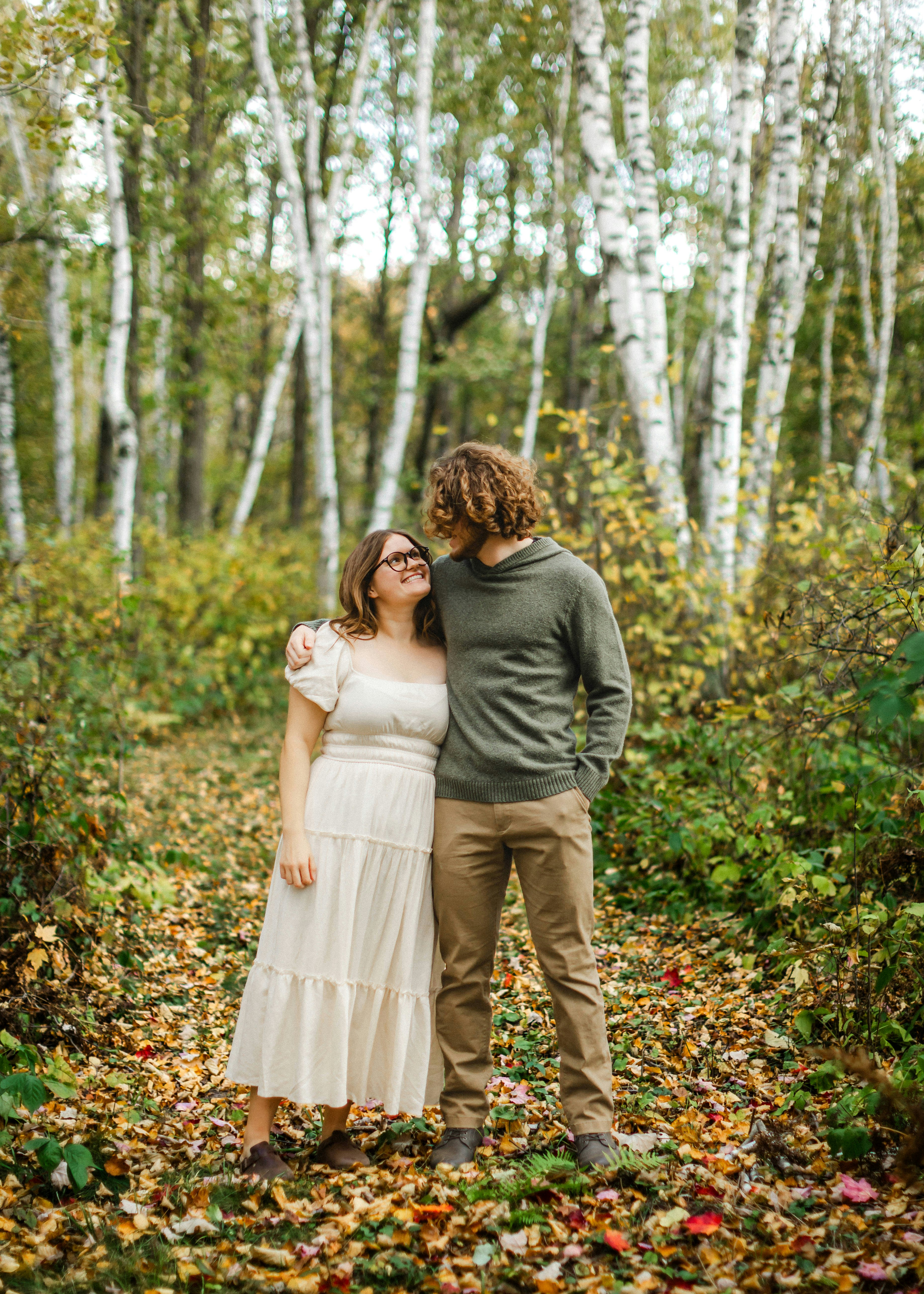 Couple embracing in a forest filled with fall foliage.