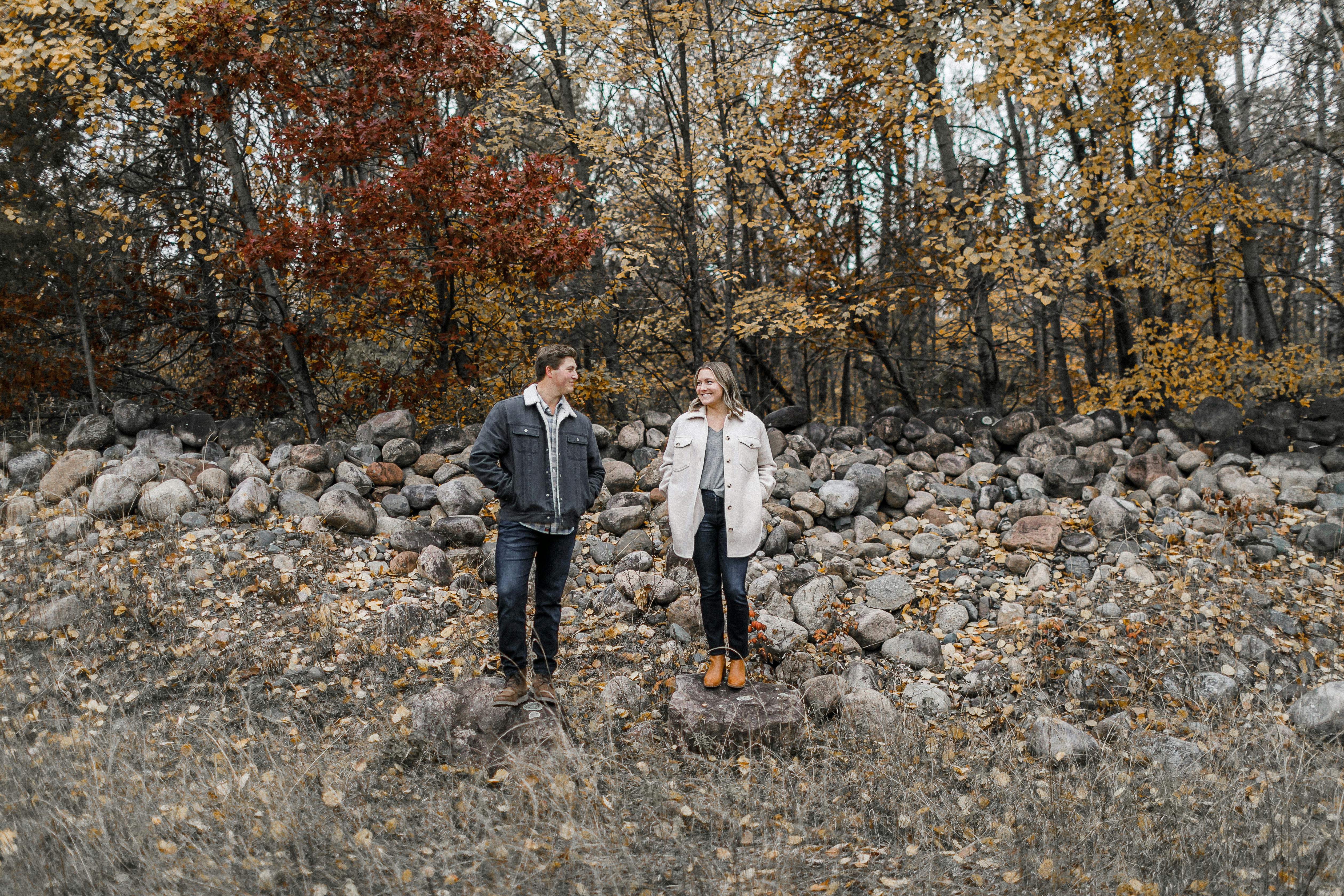 A couple smiles while standing in a forest.