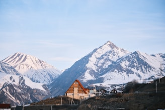 A cozy house sits before snowy mountains.