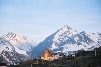 A cozy house sits before snowy mountains.