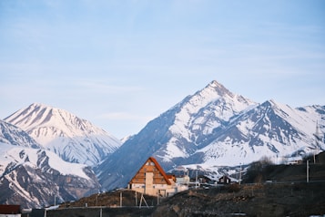 A cozy house sits before snowy mountains.