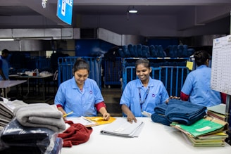 Workers sort and fold laundry in an industrial setting.