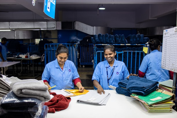 Workers sort and fold laundry in an industrial setting.