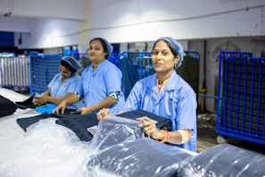 Workers prepare clothing in a factory setting.