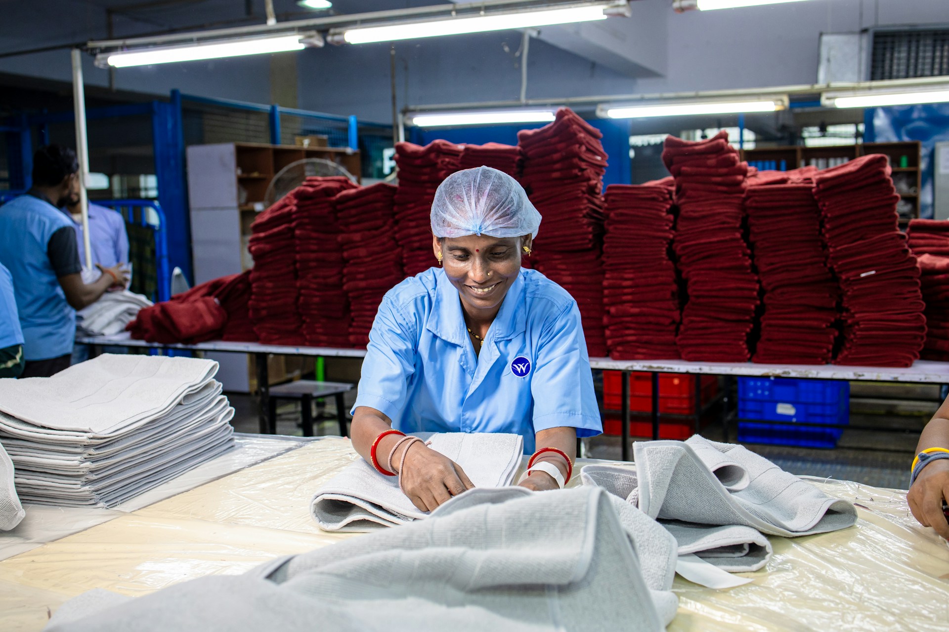 Woman folds towels in a factory setting.