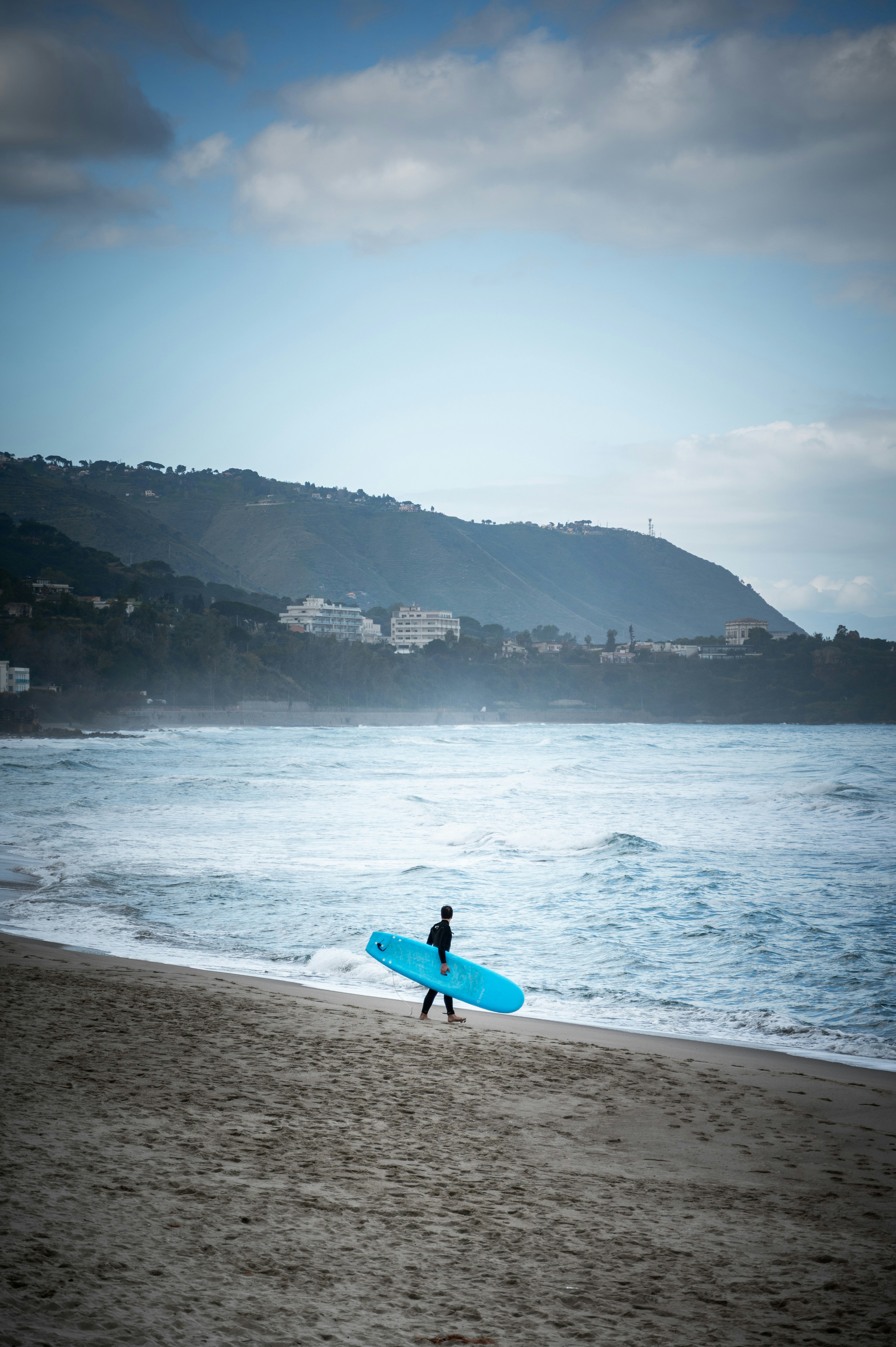 Ein Surfer läuft mit seinem Brett am Strand entlang.