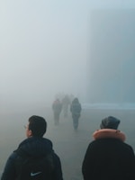 People walk through a dense, foggy atmosphere.