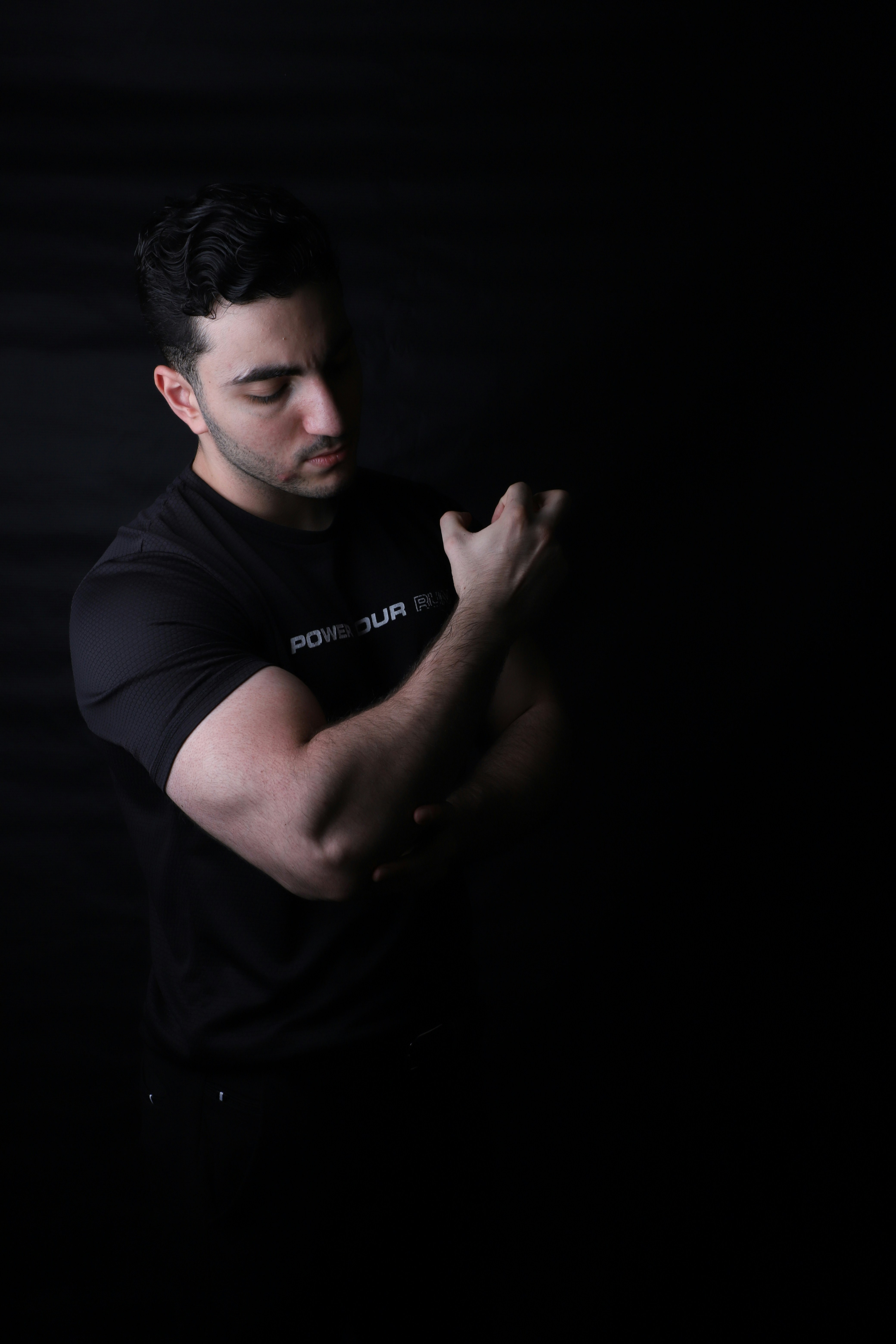 A man flexes his arm against a black backdrop.