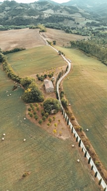 Countryside road winds past a farmhouse and fields.