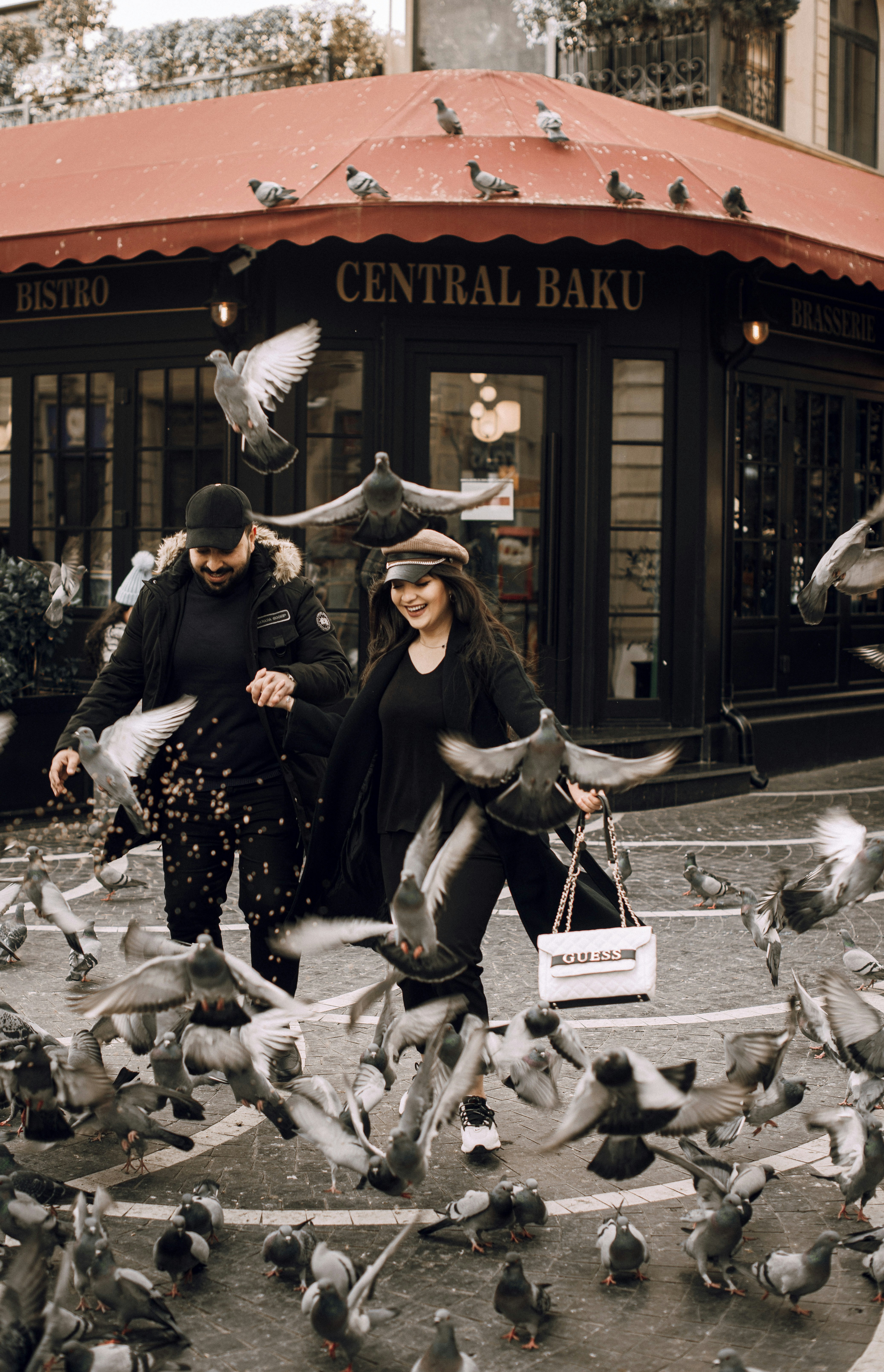 Couple surrounded by pigeons in front of a cafe.