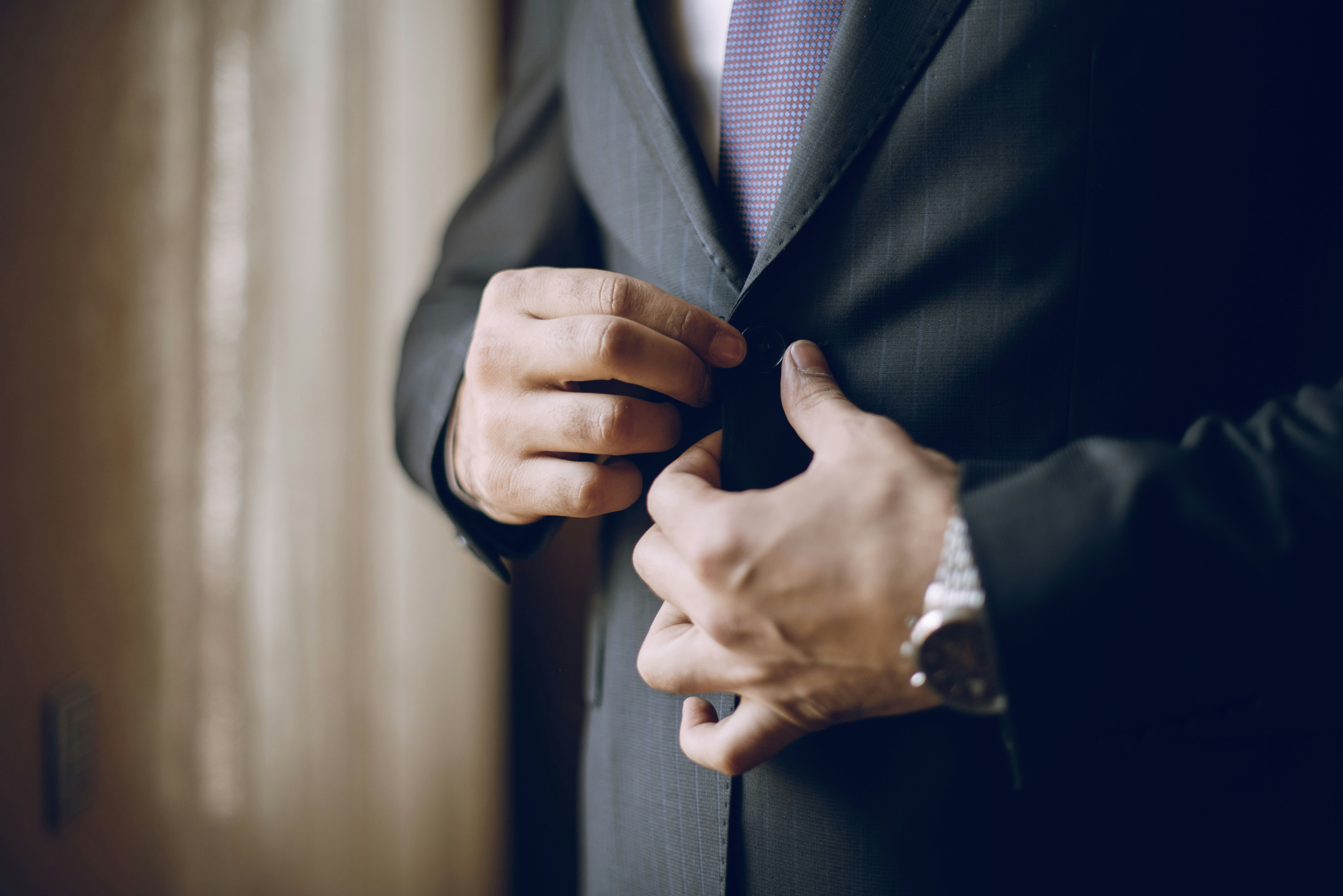 A man is buttoning his suit jacket.