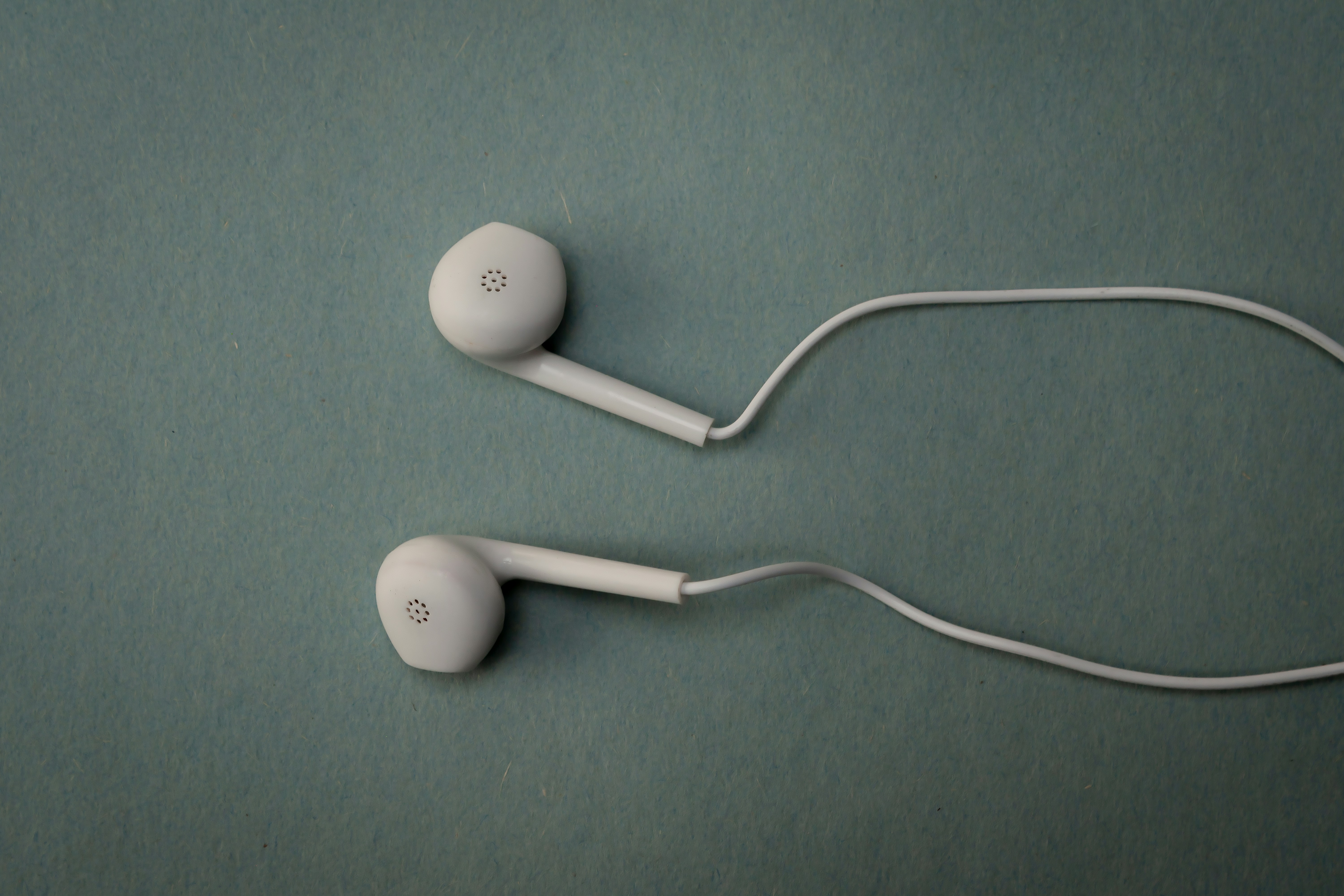 White earbuds are lying on a green surface.