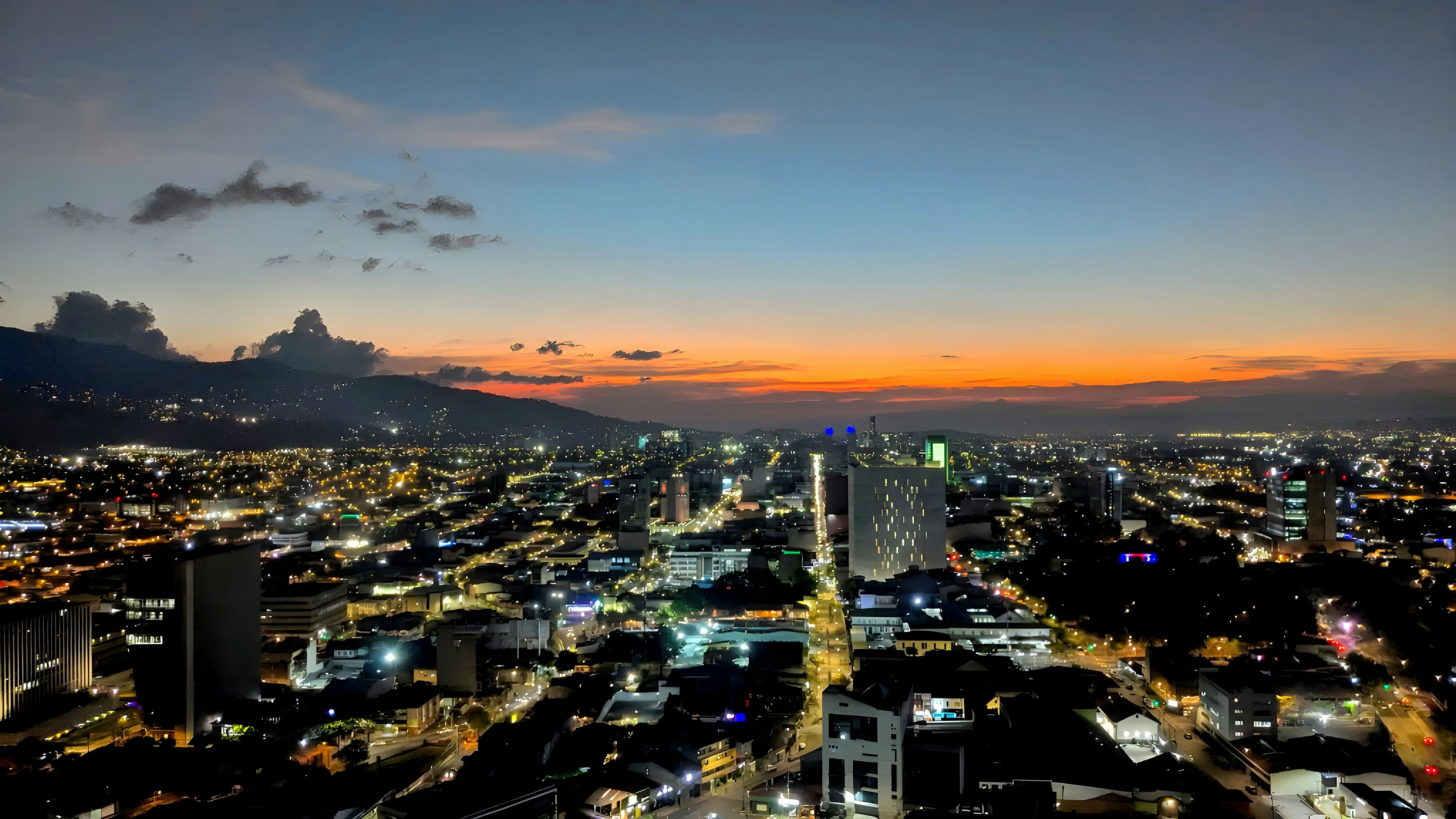 Nighttime cityscape shows lights and mountains.