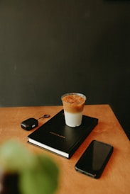 Coffee, notebook, phone, and earbuds on a table.