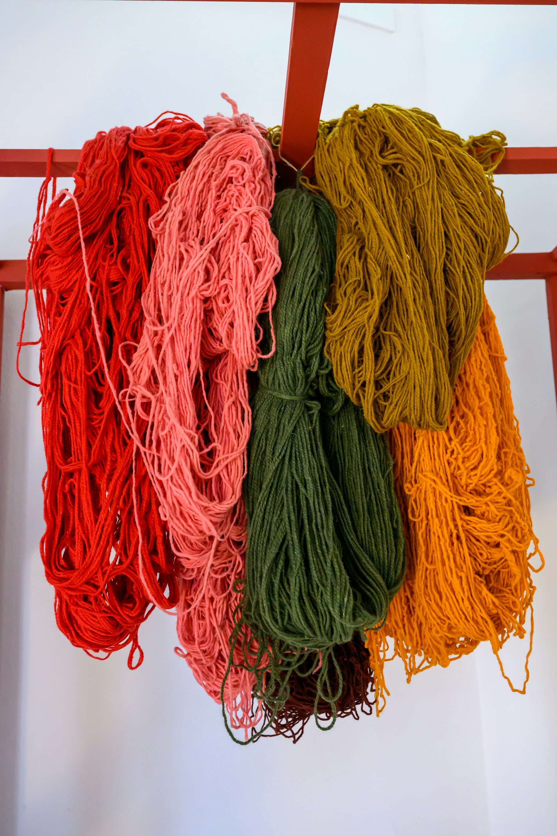 Colorful yarn hangs from a red rack.
