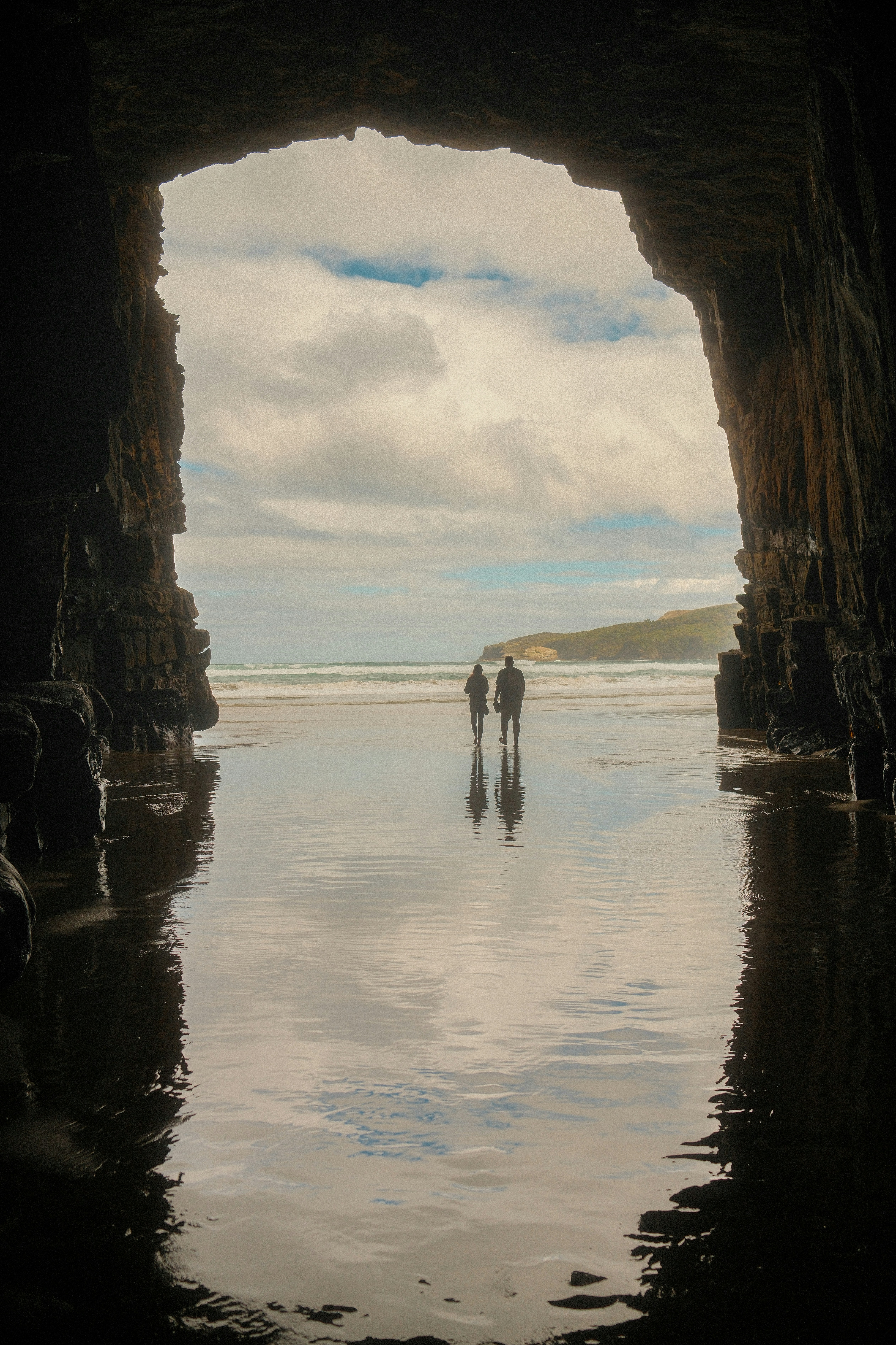 Two people explore a beach from inside a cave.