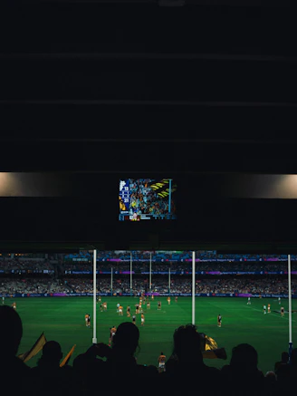 Afl game underway with stadium crowd and screen.