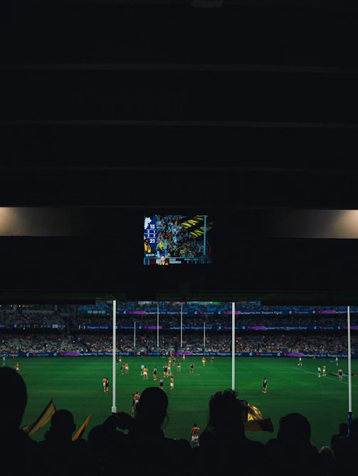 Afl game underway with stadium crowd and screen.