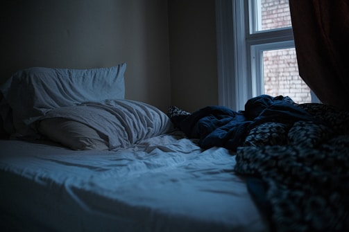 An unmade bed in a dark, quiet bedroom.