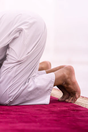 A person kneels in prayer on a rug.