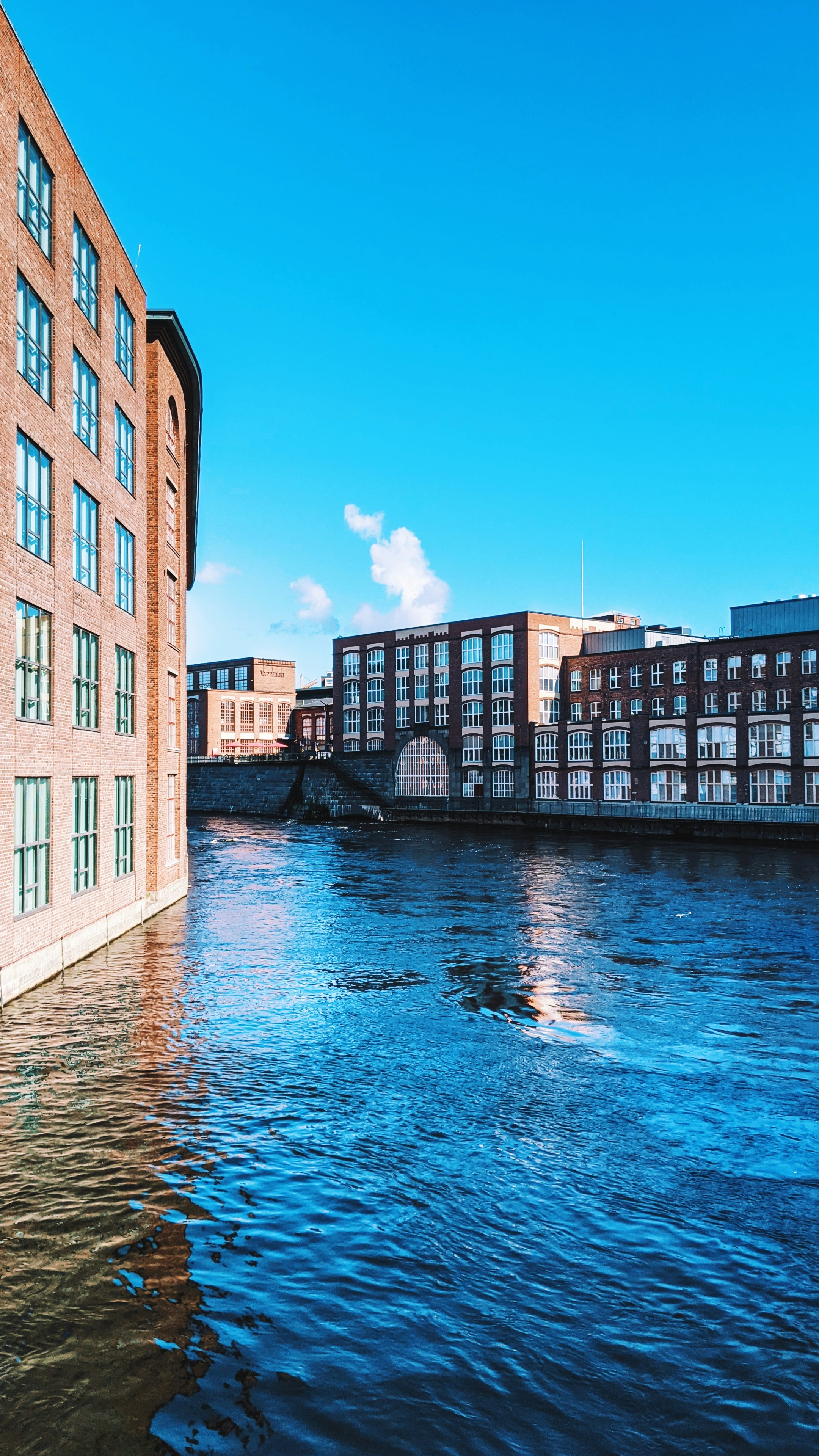 Buildings line a river under a bright, blue sky.