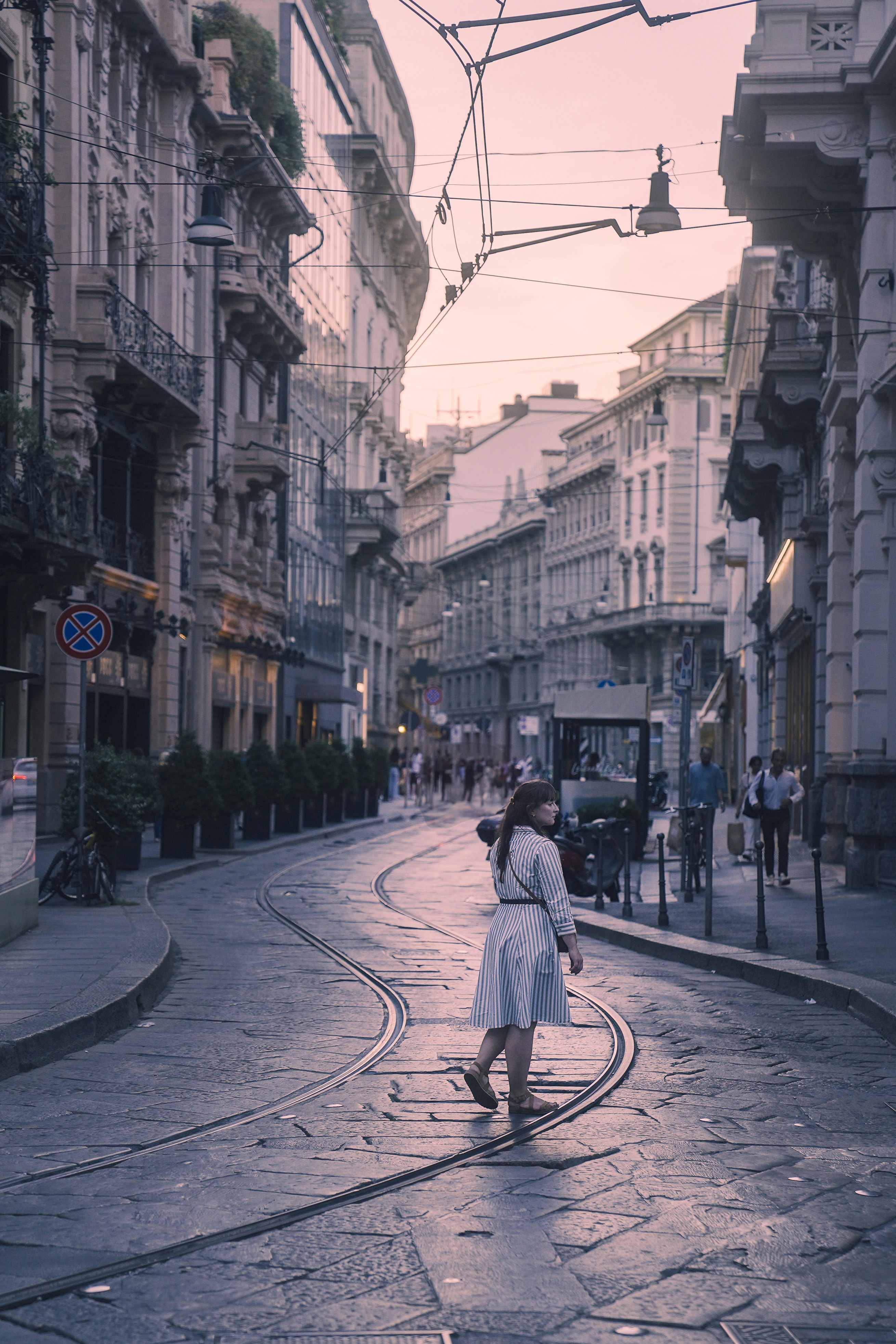 Woman walks down a cobblestone street in a city.