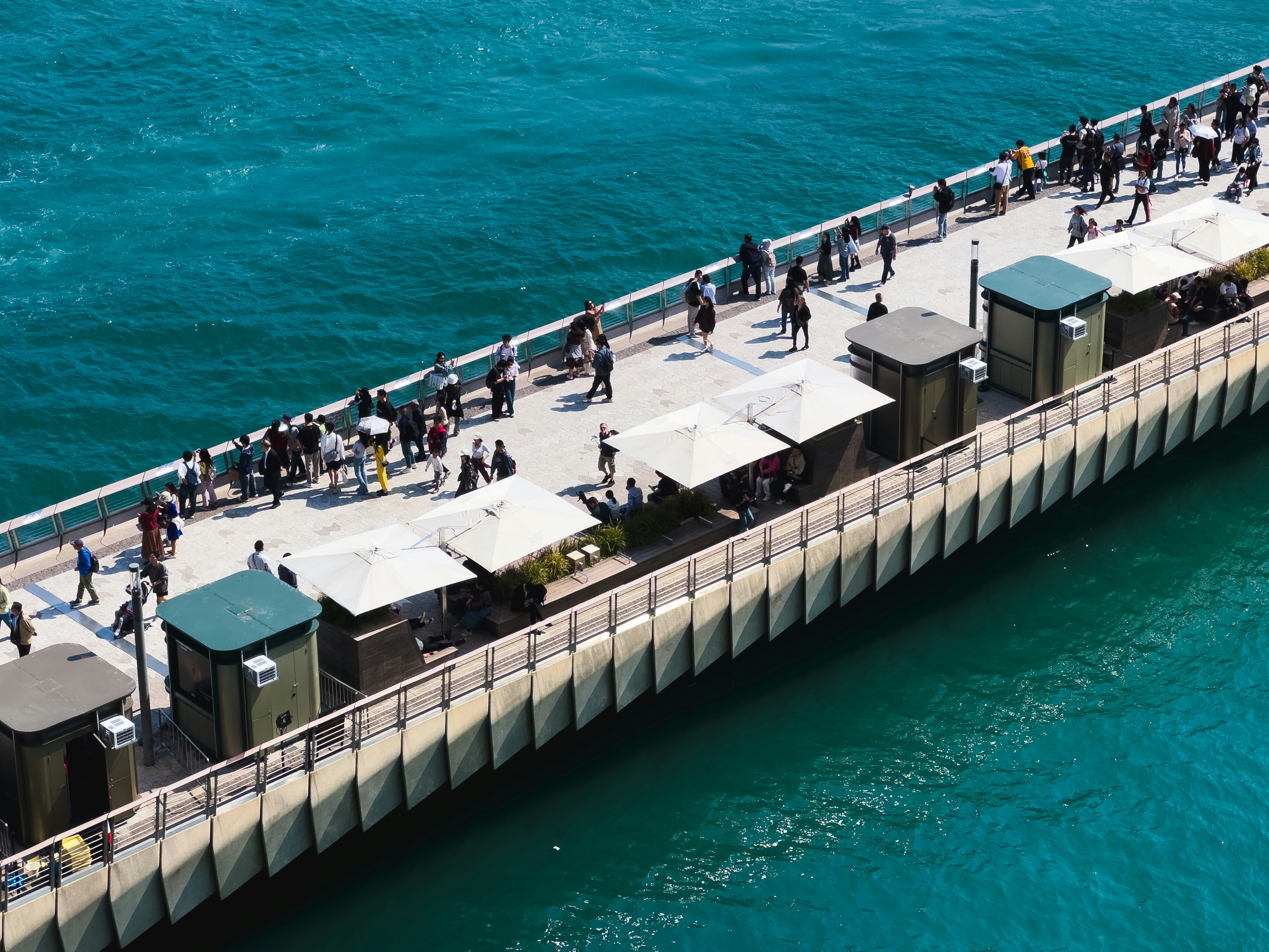 Die Menschen laufen auf einem Steg, der sich in das türkisfarbene Wasser erstreckt.