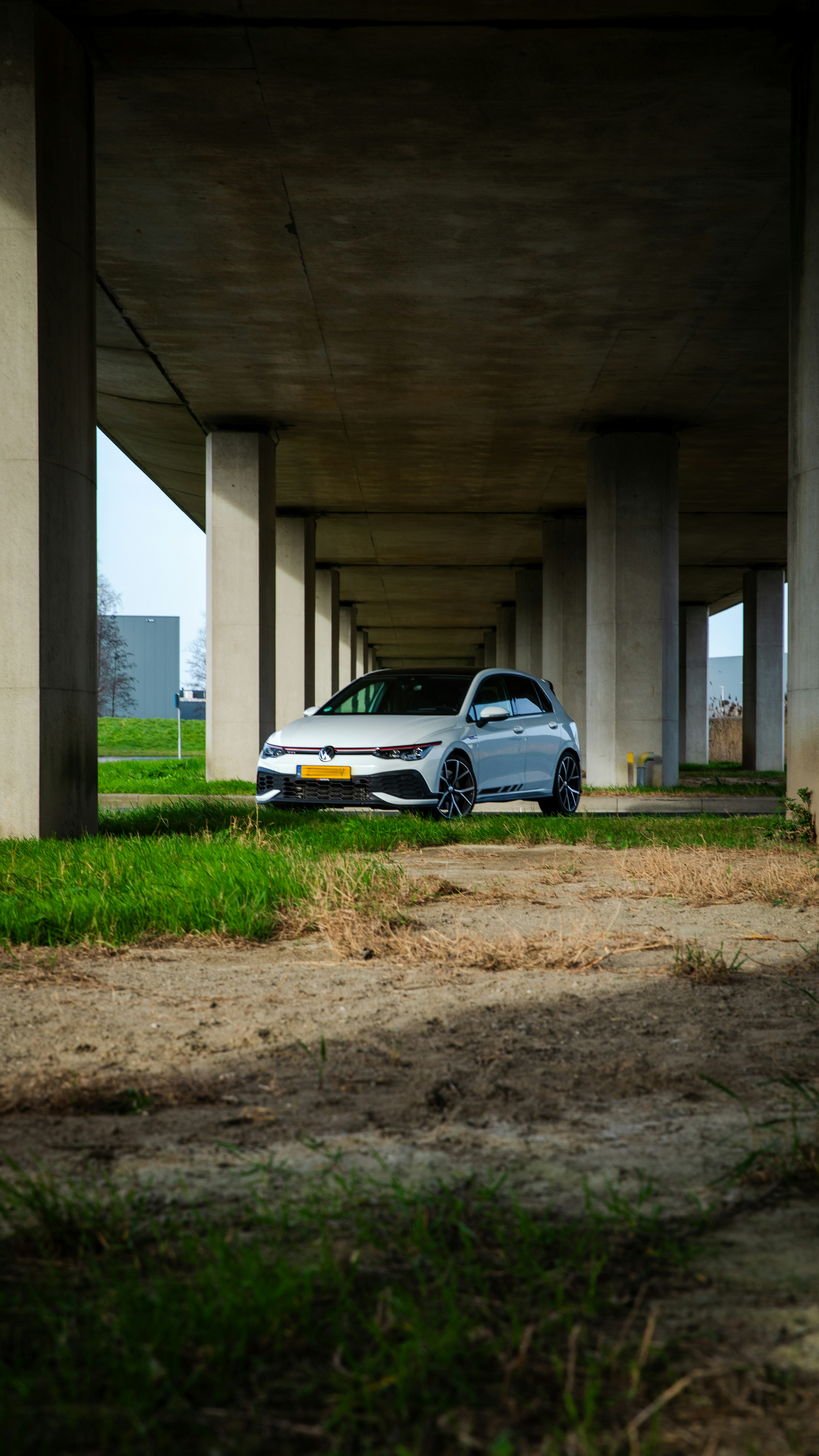 A white car parked beneath a concrete bridge.