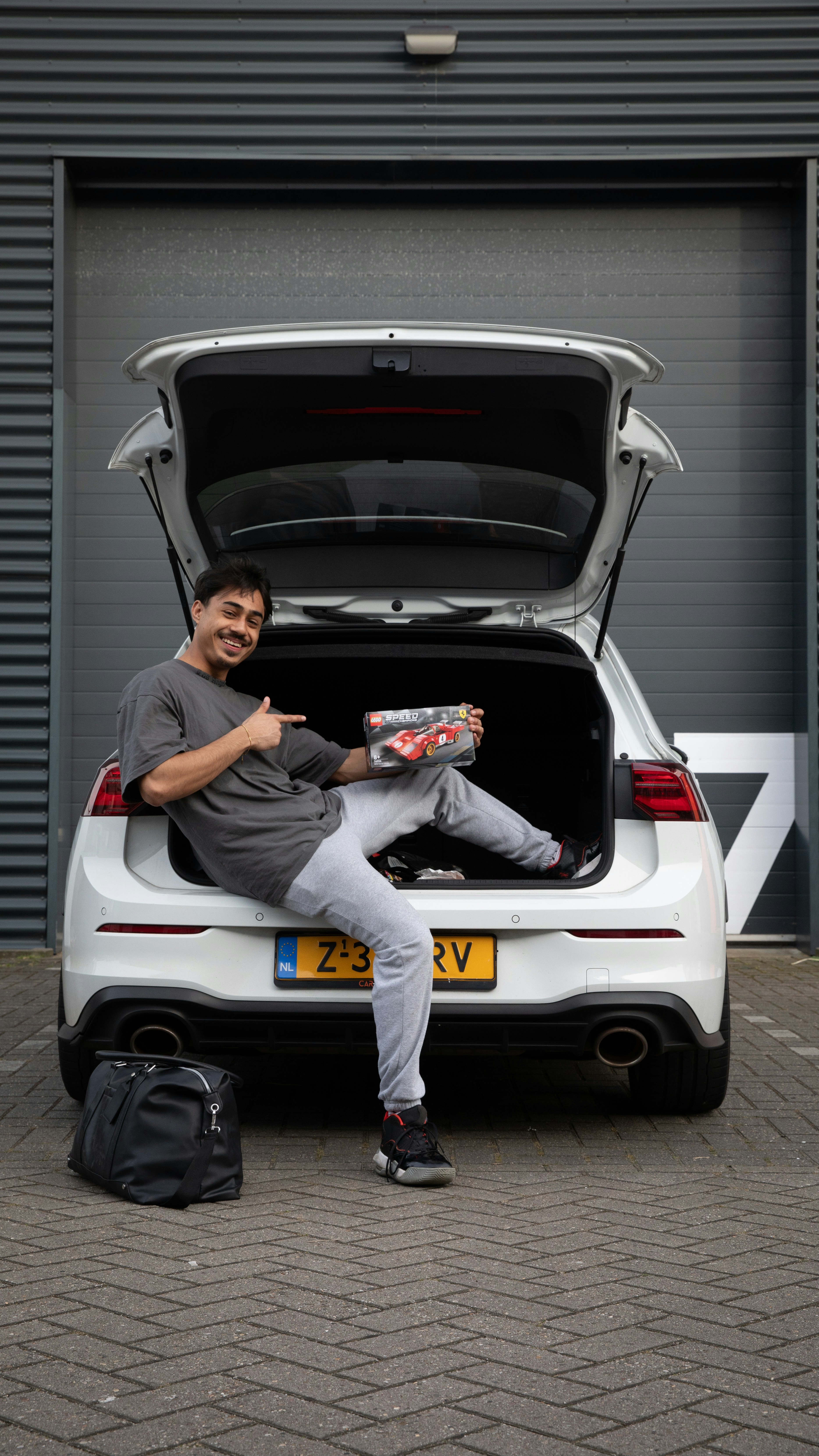 Man sits in car trunk, holding a package.