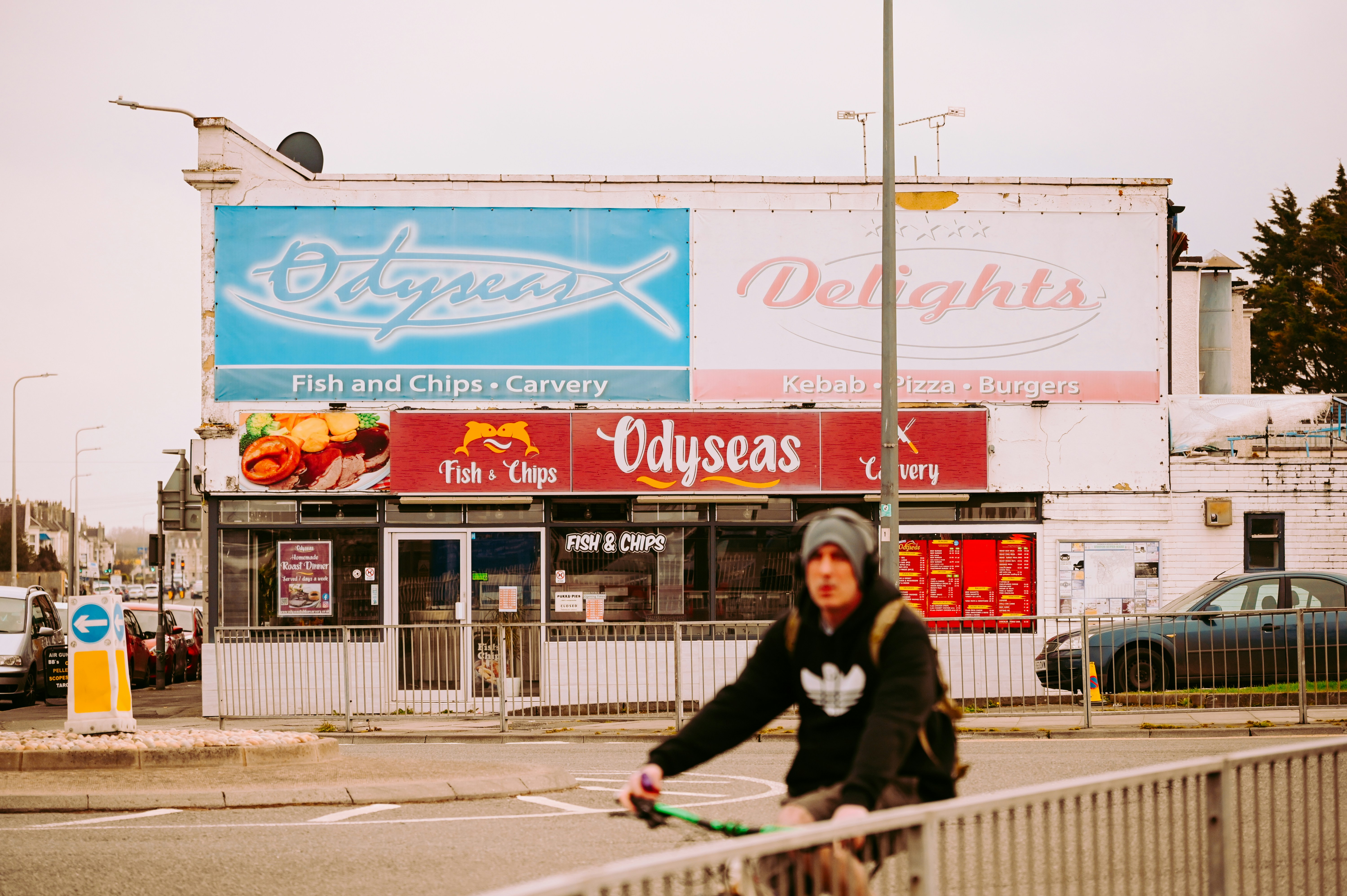 A person cycles past a fish and chip shop.