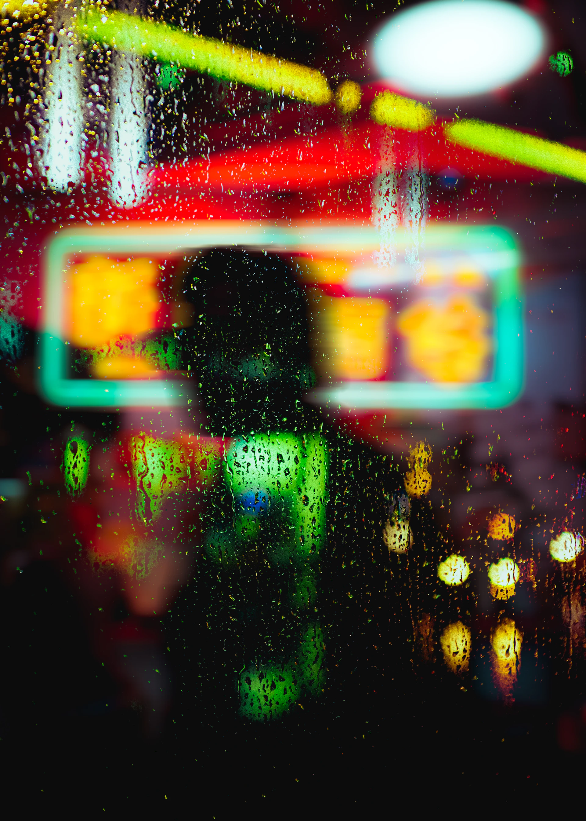 Raindrops blur neon lights in a nighttime scene.