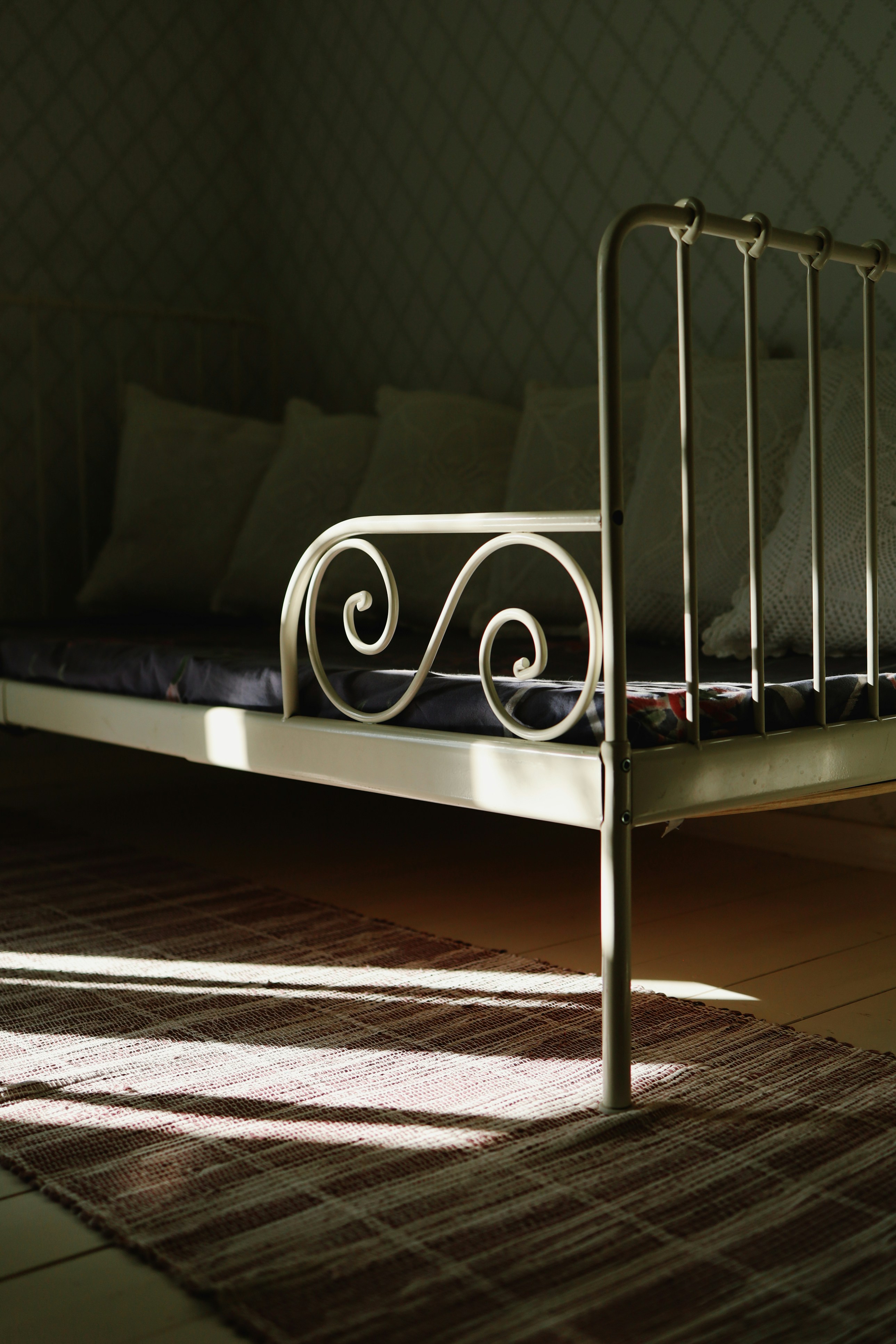 A bed sits peacefully in sunlit shadows.