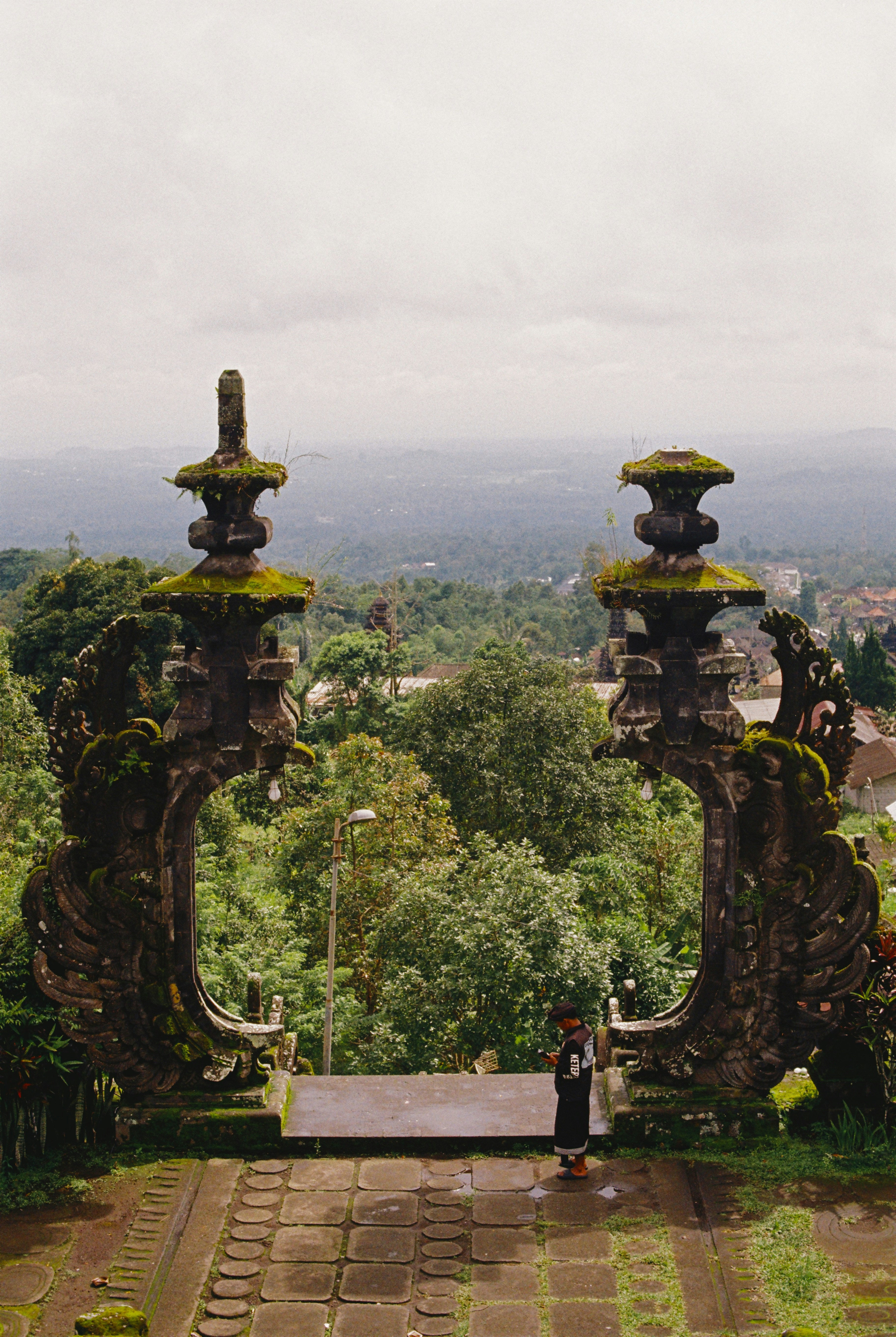 Gerbang batu membingkai tanaman hijau subur dan langit mendung.