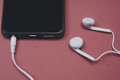 Phone and earbuds resting on a pink surface.