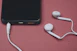 Phone and earbuds resting on a pink surface.
