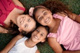 Three happy girls are smiling and lying on the grass.