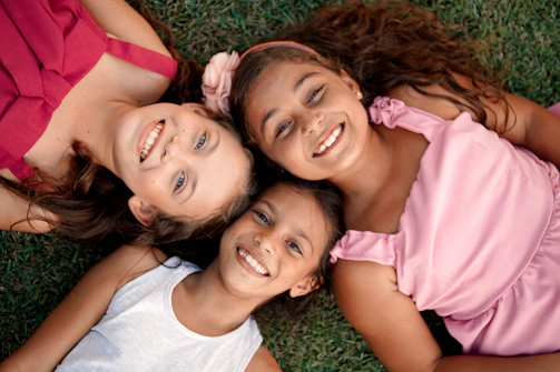 Three happy girls are smiling and lying on the grass.