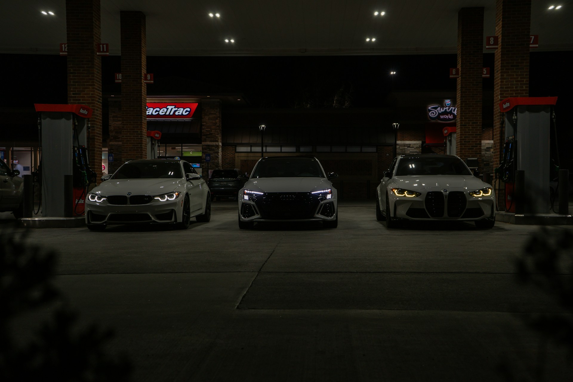 Three cars are parked at a gas station at night.