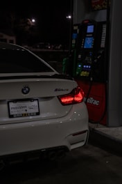 A white BMW m4 is refueling at night.
