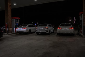 Three white cars are at a gas station.