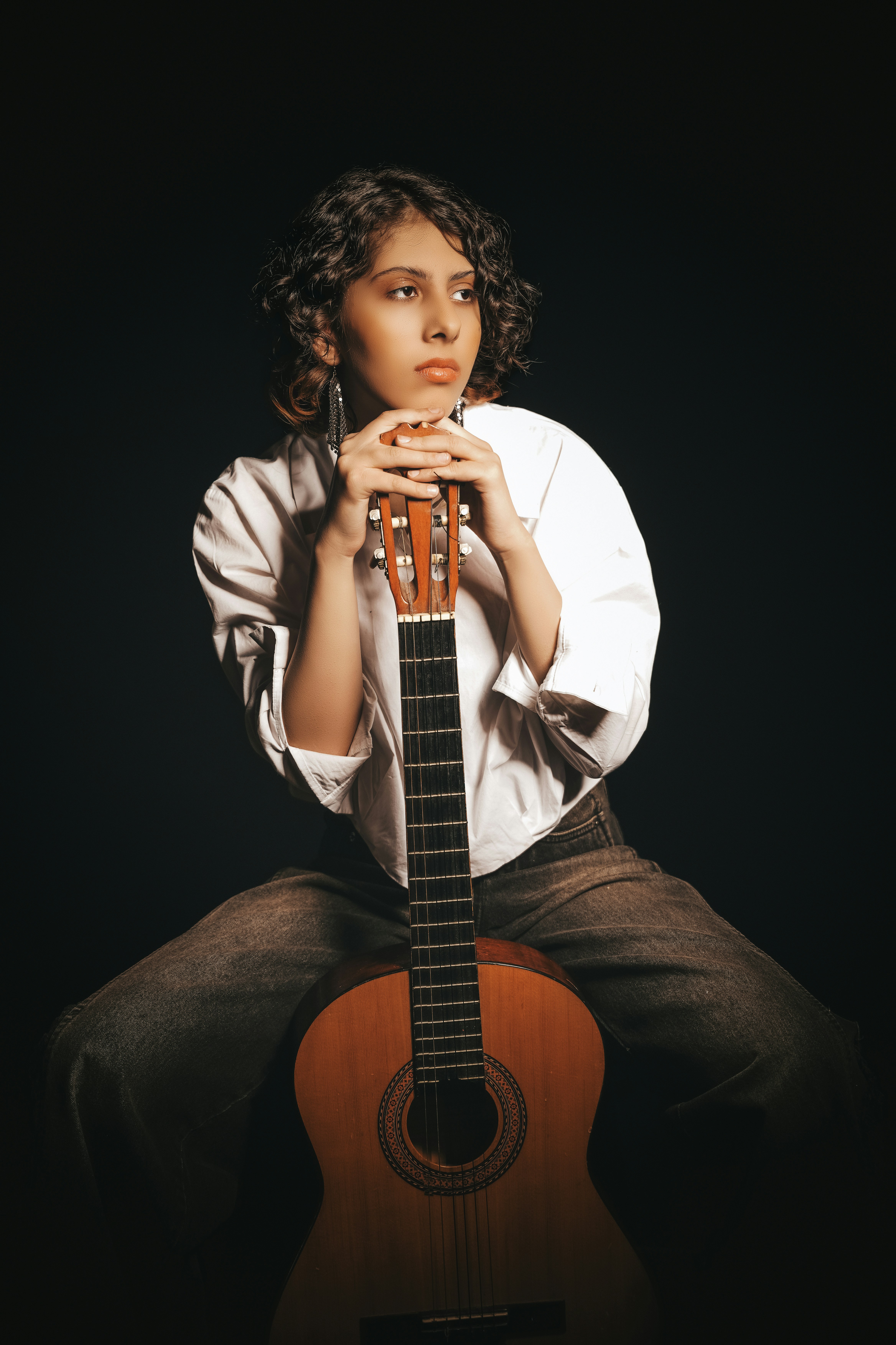Girl poses thoughtfully with a classical guitar.