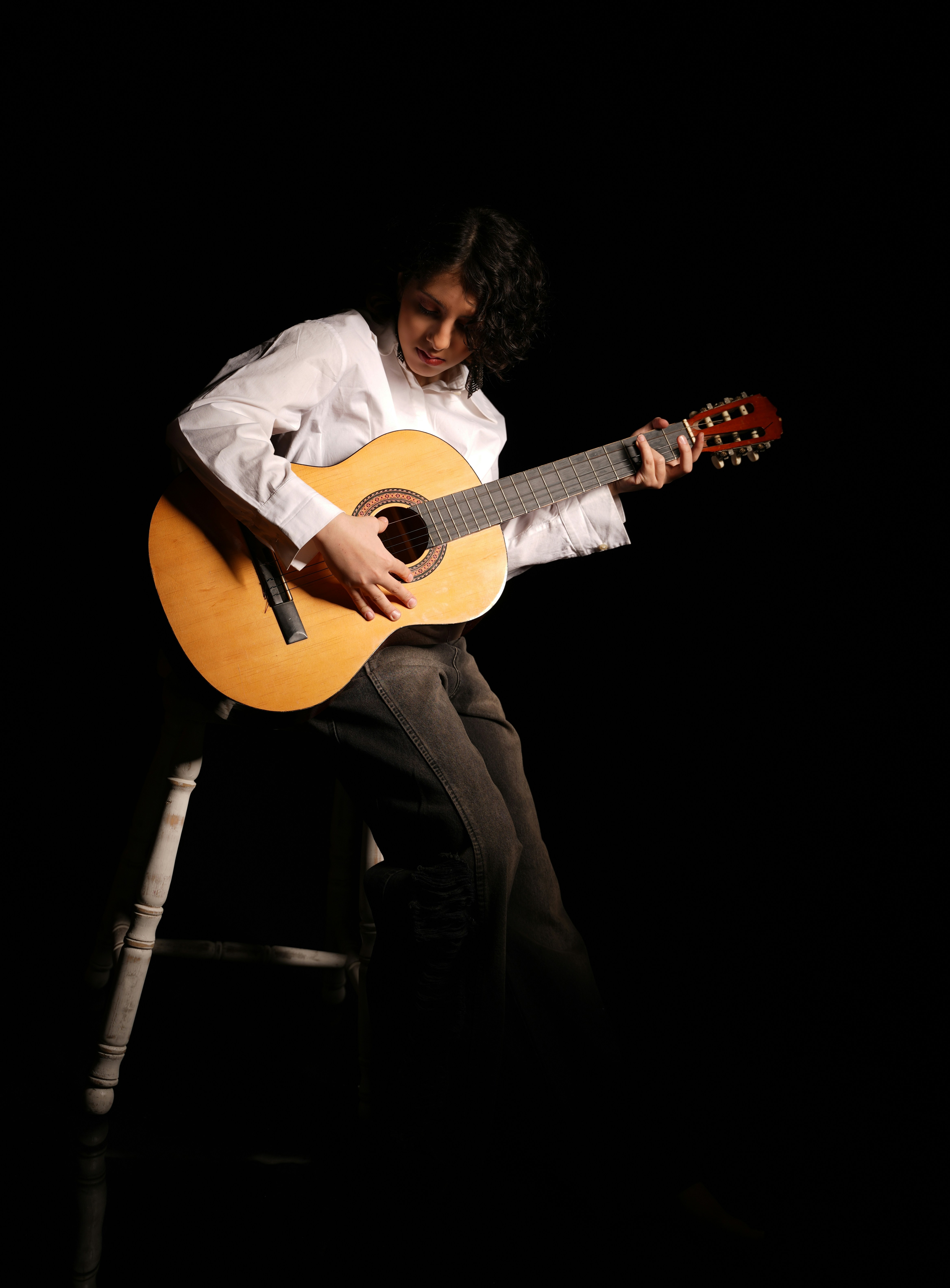 Person plays acoustic guitar on a stool.
