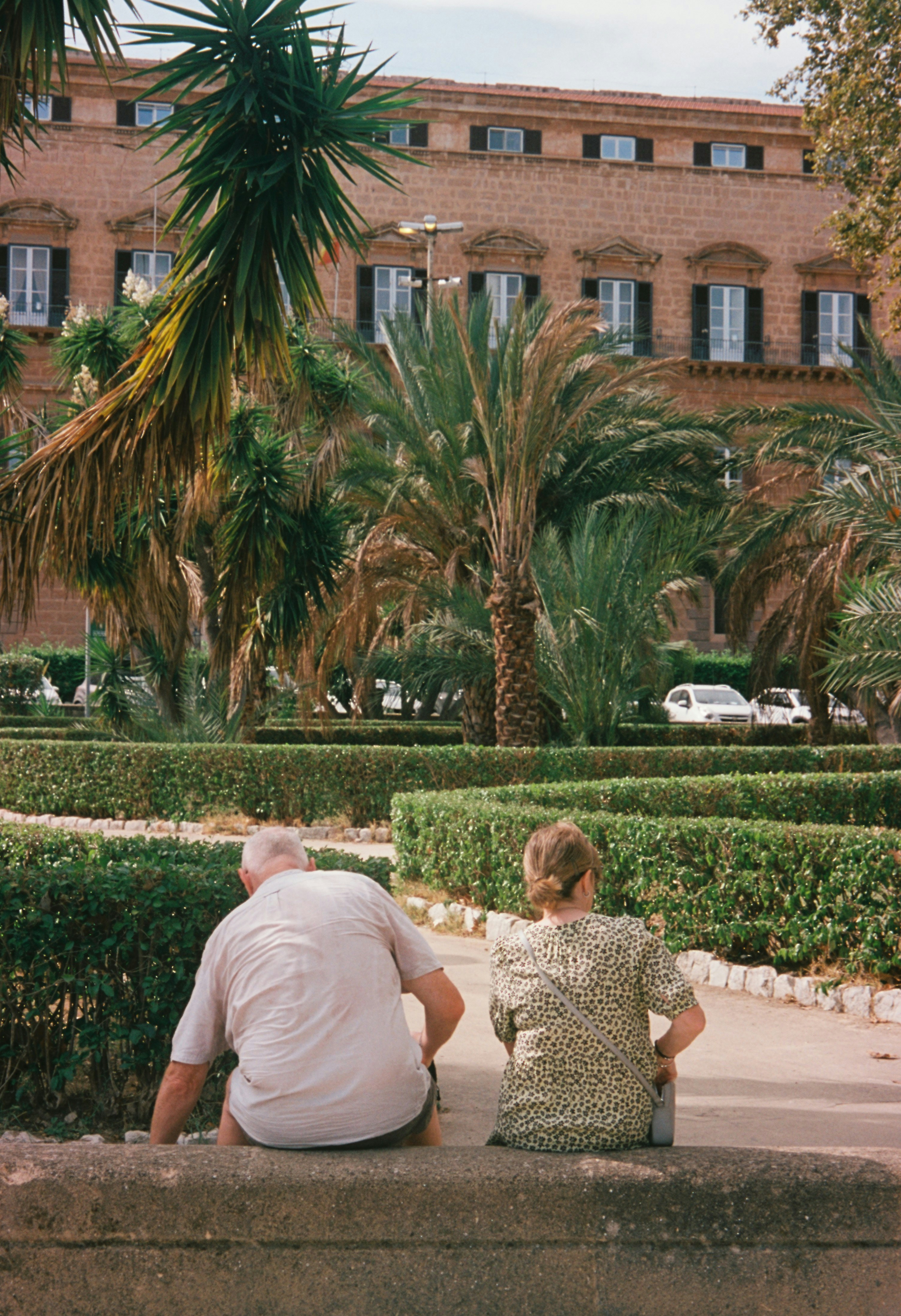 Couple sits looking at a park and a building.
