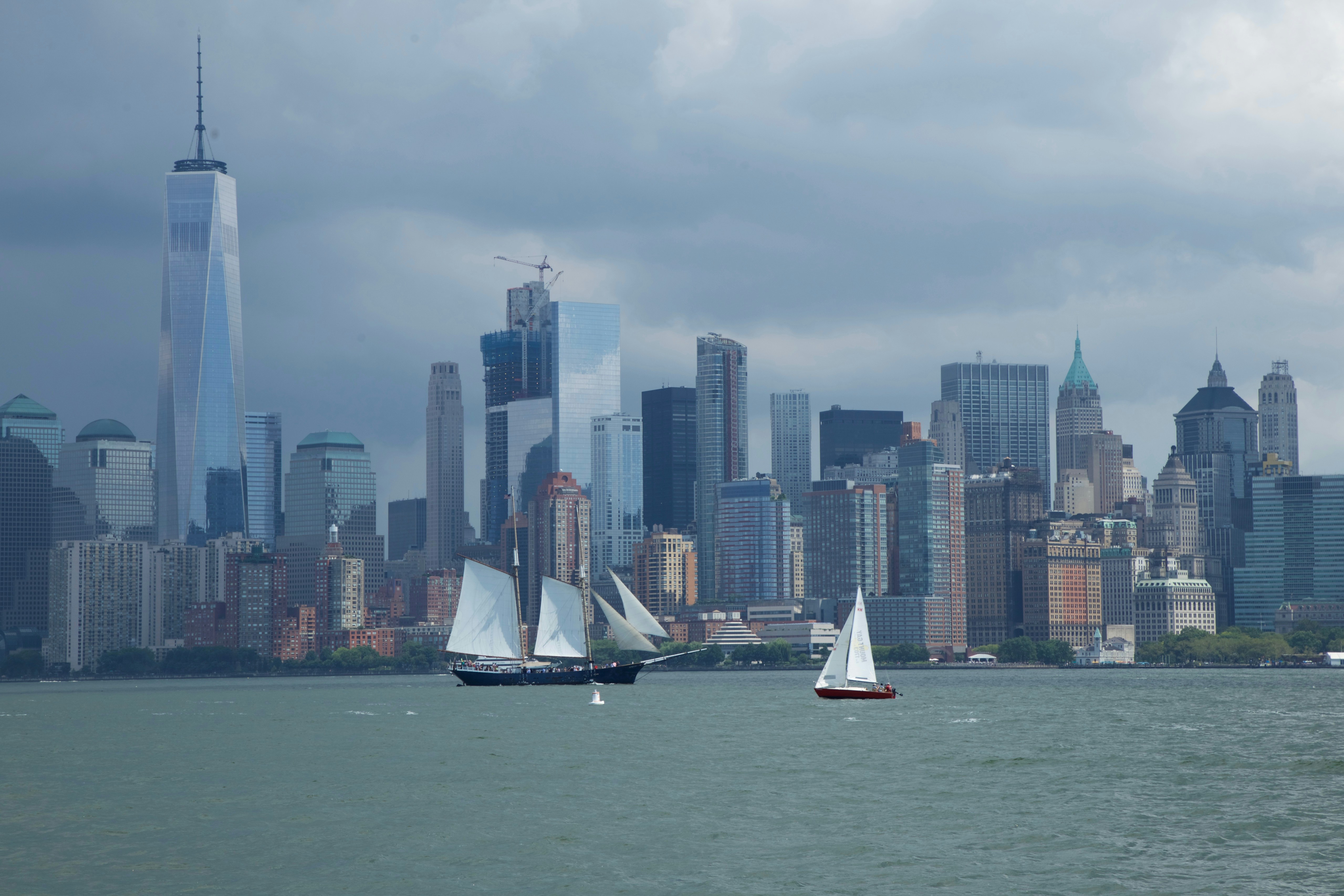 Sailboats navigate in front of the new york city skyline.