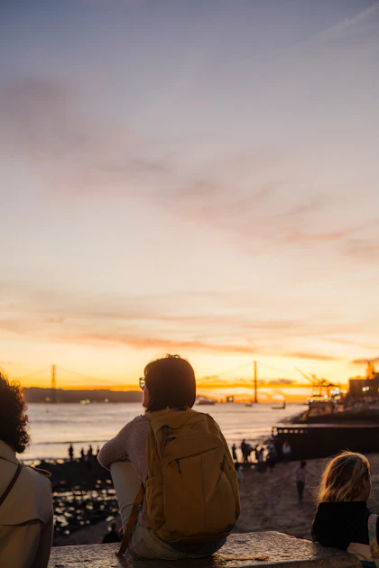 Mulher sentada à beira-mar vendo o pôr do sol em Lisboa