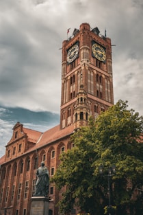A brick tower with clocks and a cloudy sky.