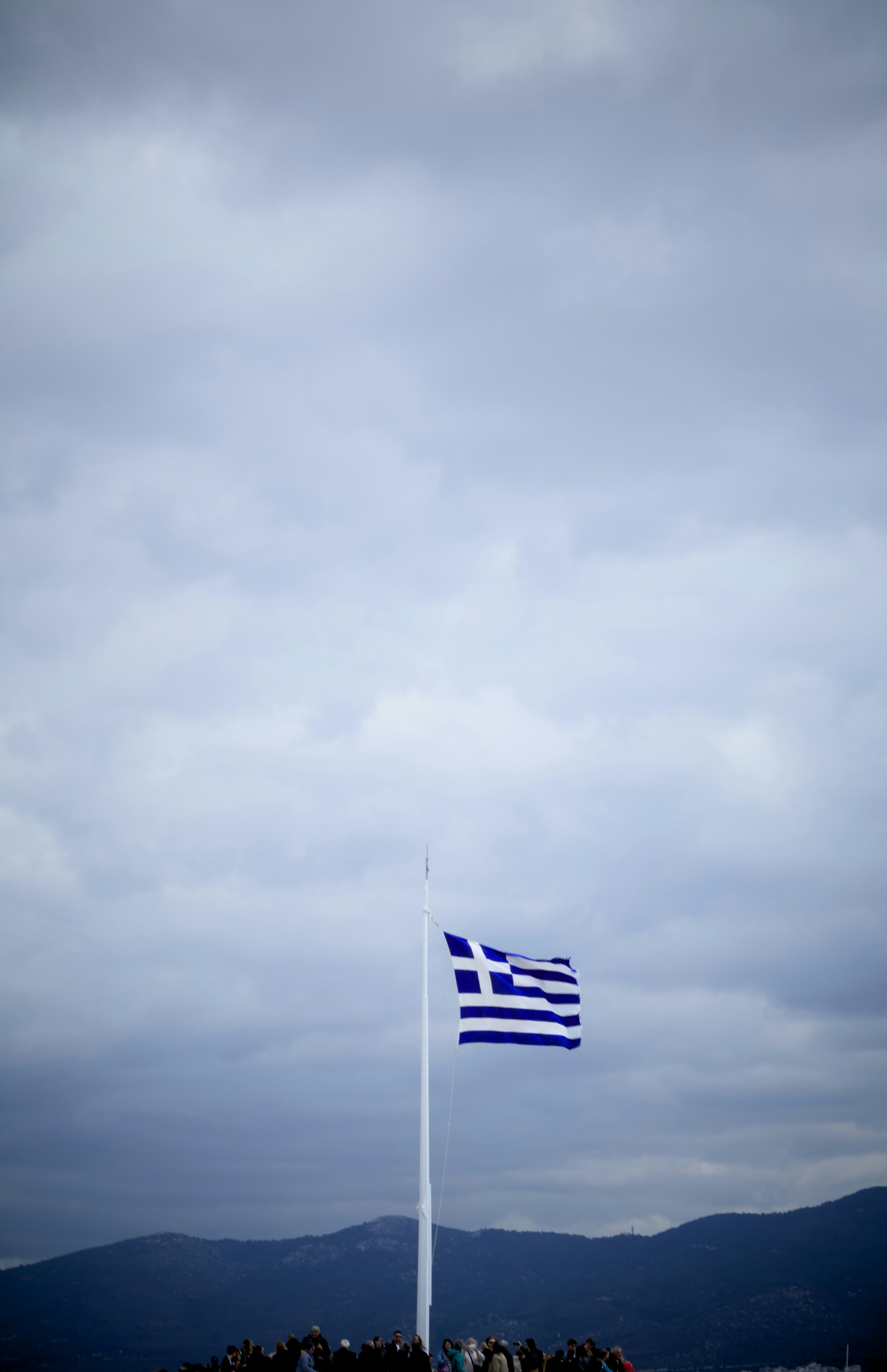 The greek flag flies at half-mast under cloudy skies.