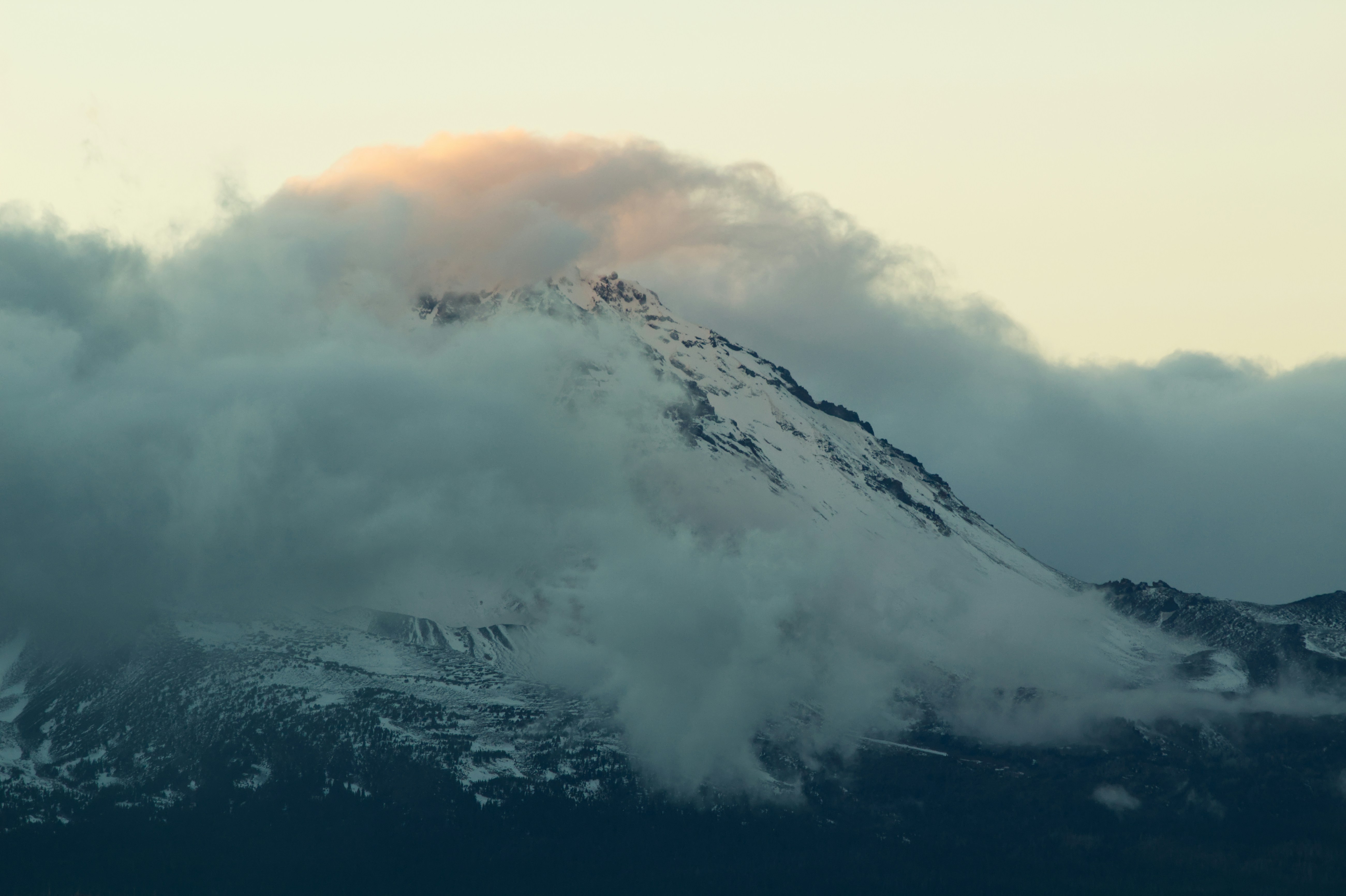 Clouds engulf a snow-covered mountain peak.