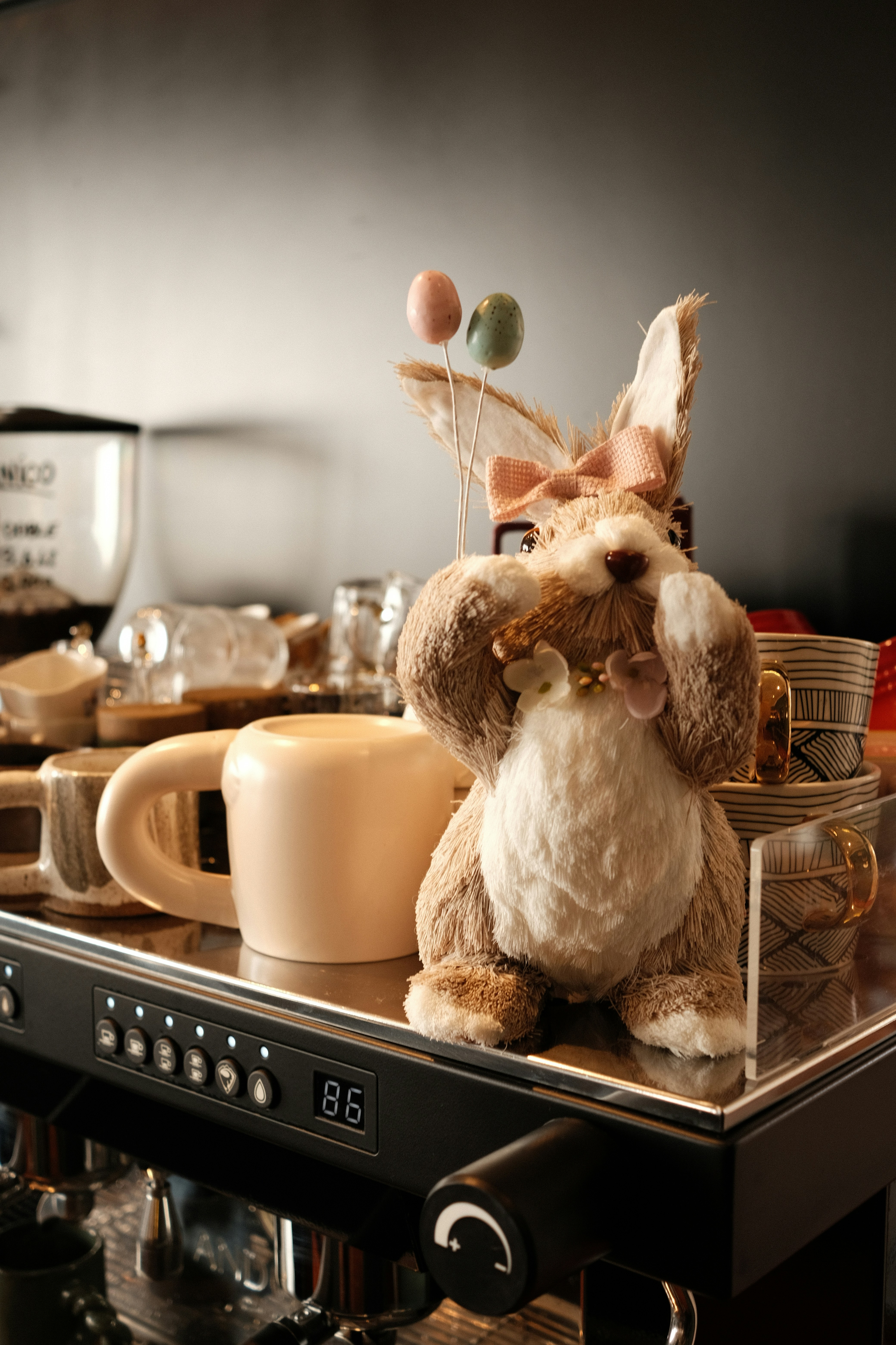 Easter bunny with balloons sits by coffee machine.