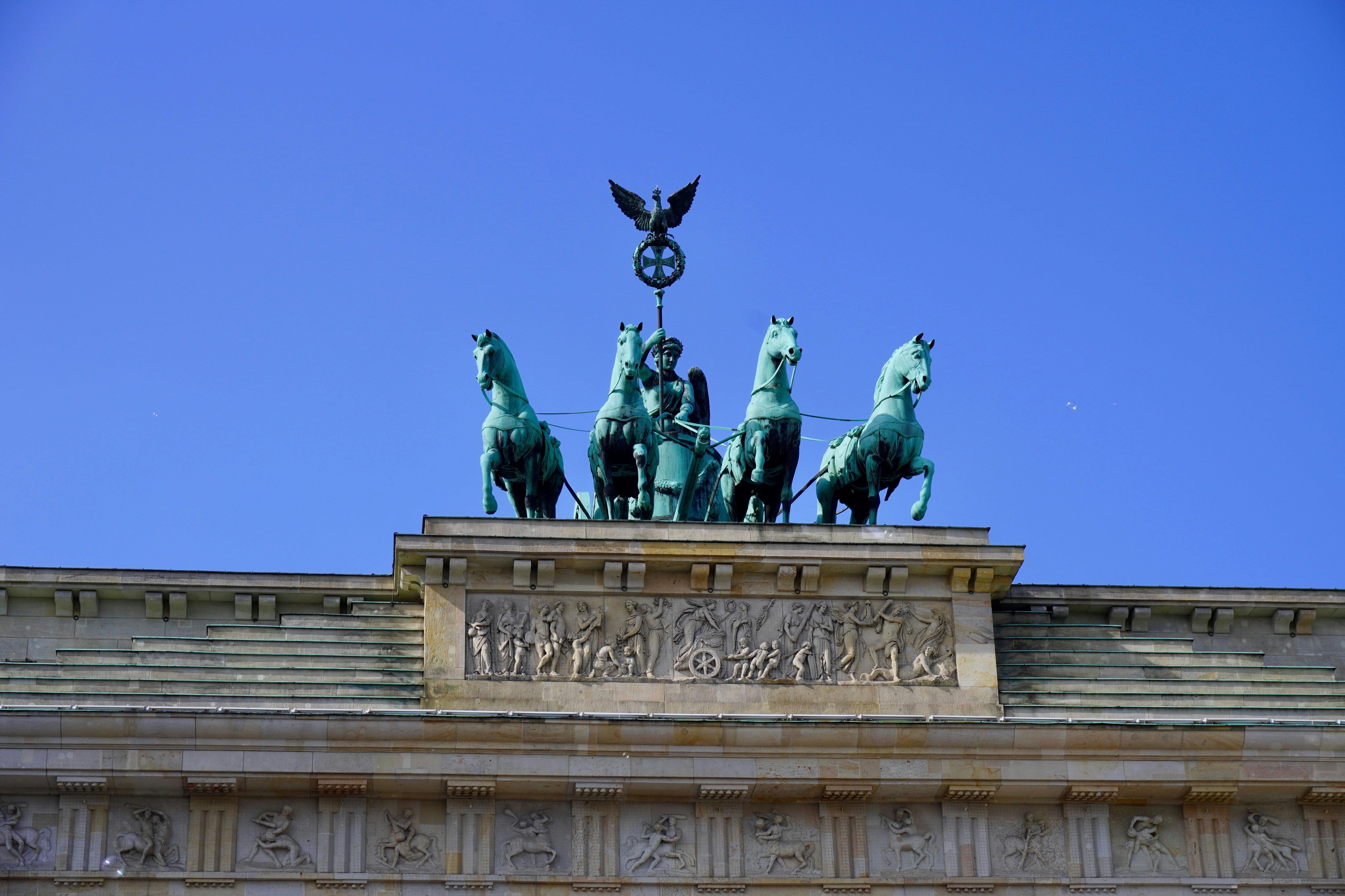 The brandenburg gate statue is displayed against blue sky.